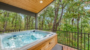 Een hottub op een houten terras met uitzicht op een bos.