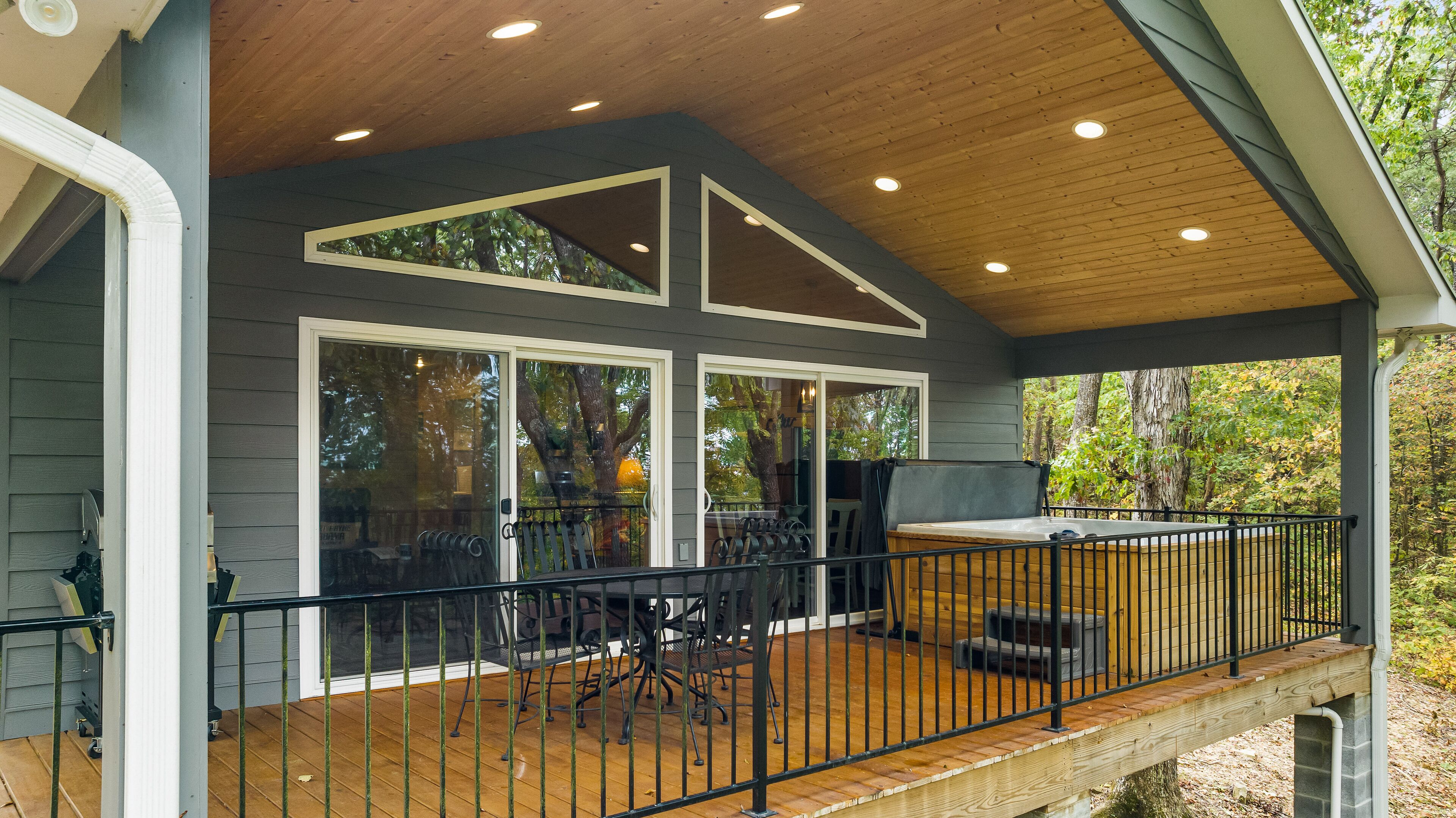 A covered patio with a wooden deck, a hot tub, and a seating area with chairs and tables.