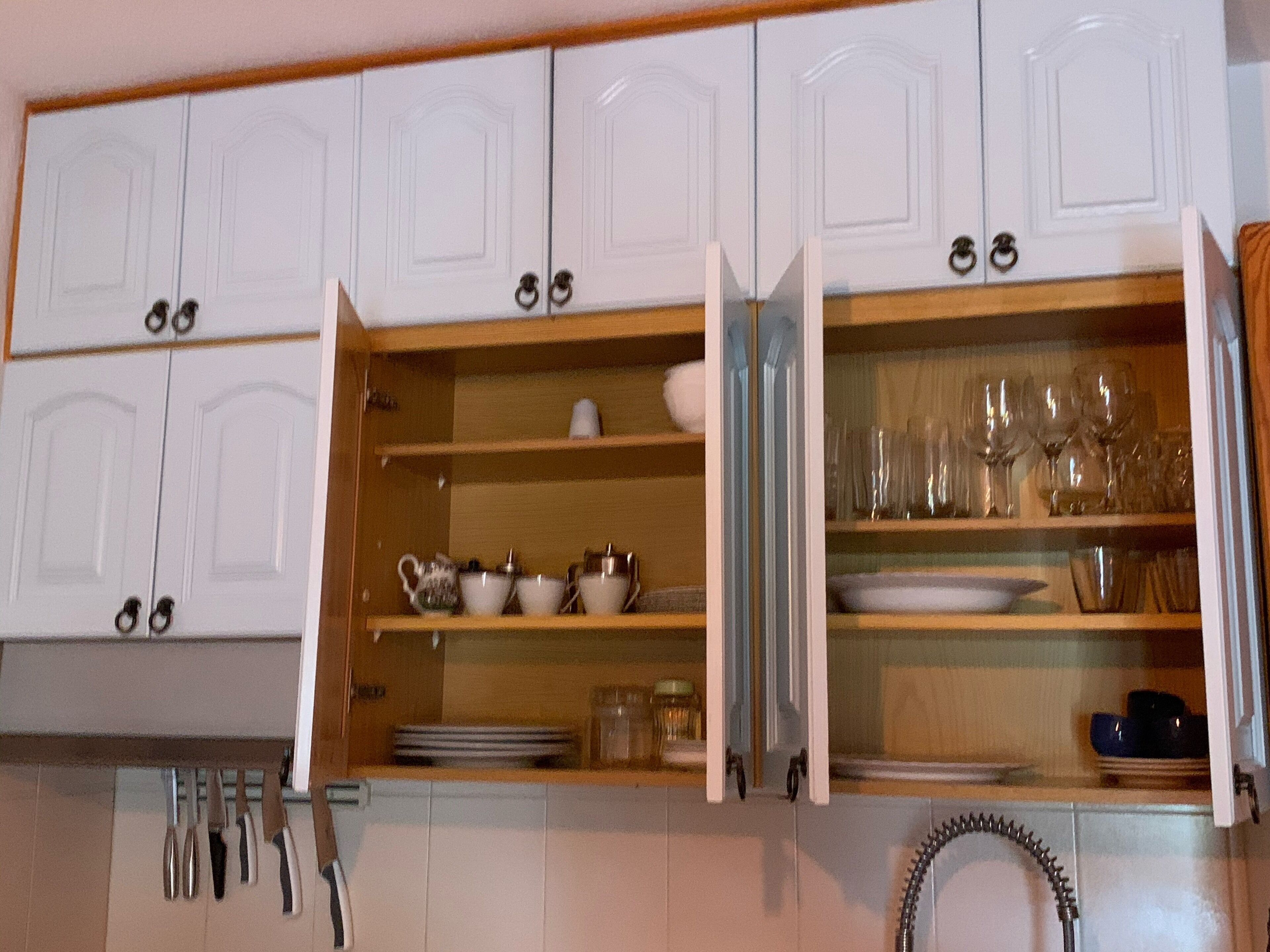 A kitchen with white cabinets, open shelves with dishes and utensils, and a stainless steel sink.
