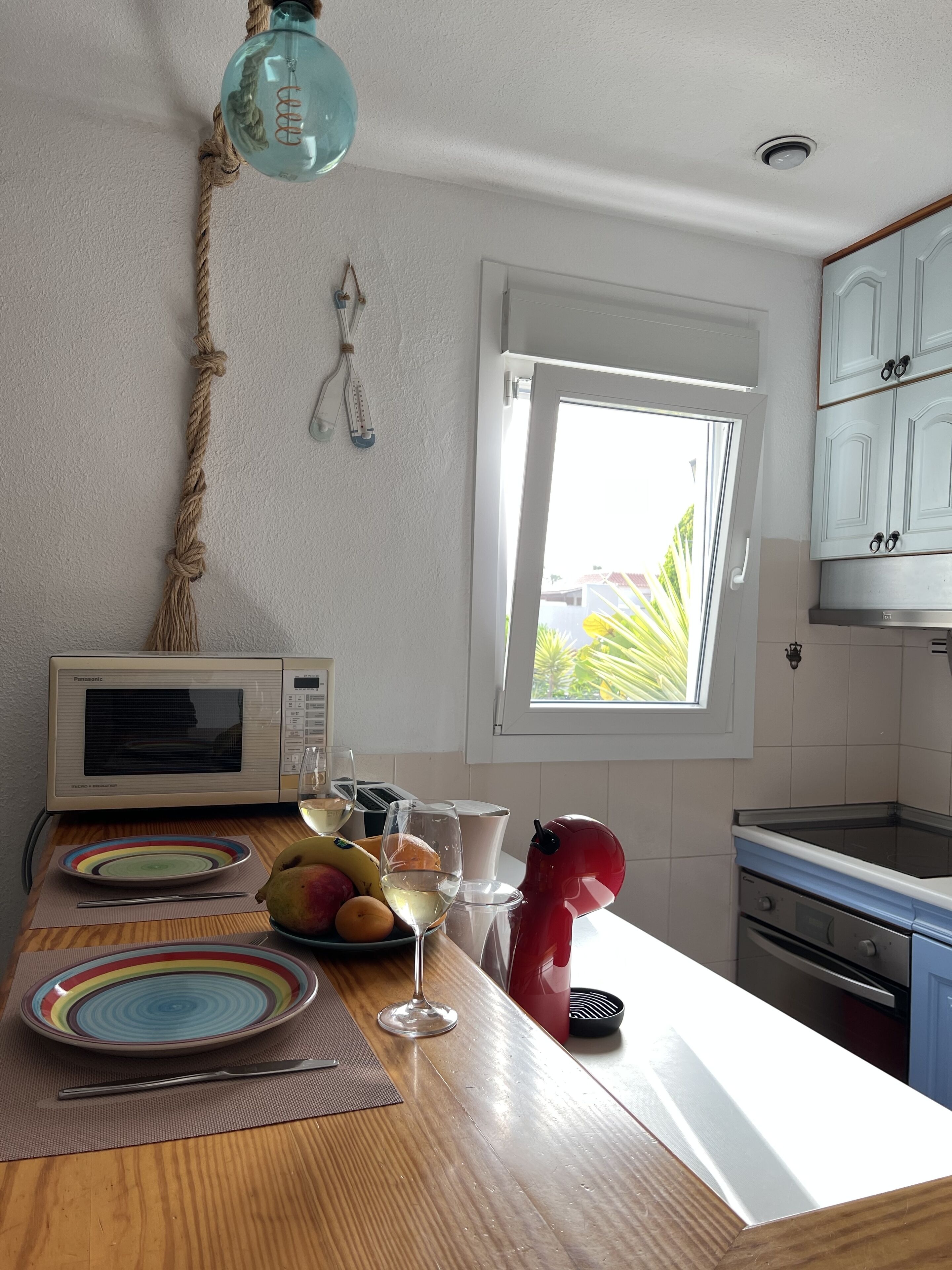 A kitchen with a wooden countertop, a microwave, a fruit bowl, a wine glass, and a red toaster.