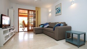 A living room with a sectional sofa, a television, a small table, and a door leading to an outdoor area.