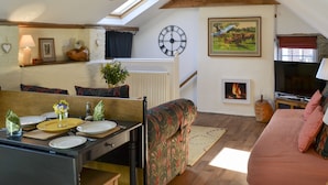 A cozy living room with a high ceiling, wooden beams, a dining area with a table set for two, a sofa, and a fireplace. - 1 bedroom accommodation in Nordham, near Beverley (Nordham, near Beverley)