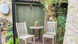 A small outdoor seating area with two wooden chairs and a round table, surrounded by a green fence and a stone wall. - 1 bedroom accommodation in Nordham, near Beverley (Nordham, near Beverley)