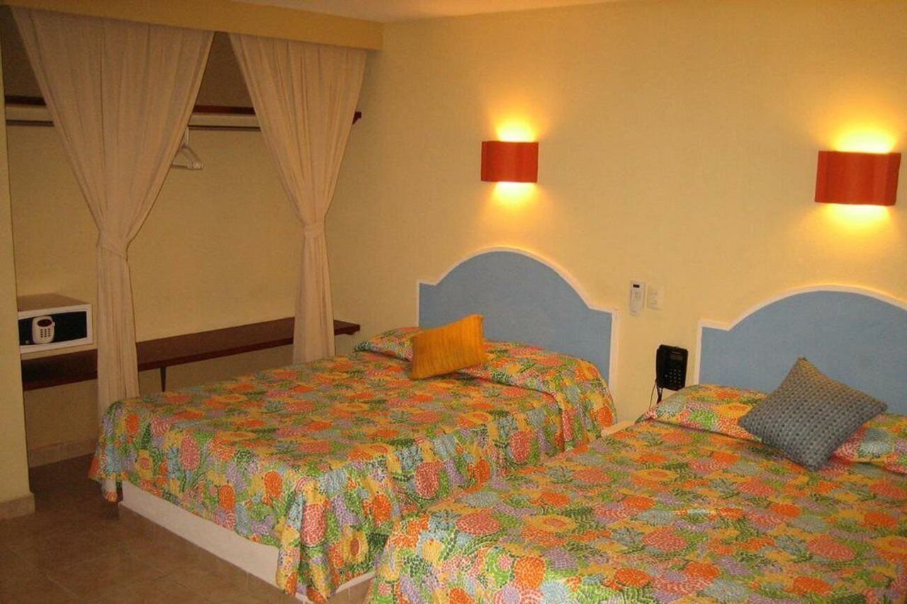 Habitación de hotel con dos camas, cada una con una colcha floral de colores, una mesita de noche pequeña, un teléfono y una lámpara de pared.