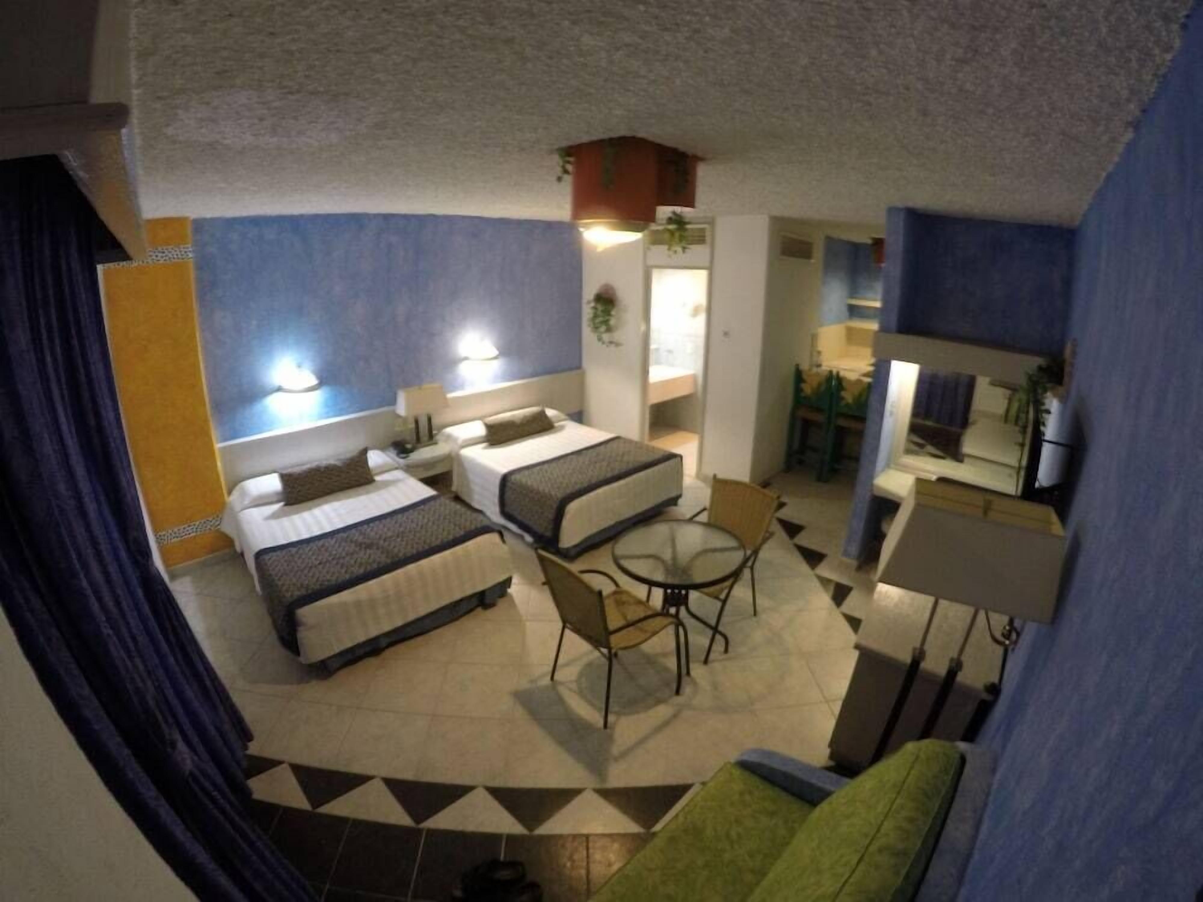 A hotel room with two beds, a small dining area, and a kitchenette.