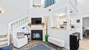 Uma sala de estar moderna com lareira, televisão e escada que leva a um andar superior.
