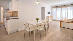 Un salon moderne et bien éclairé, comprenant un coin repas, une cuisine et un téléviseur fixé au mur.