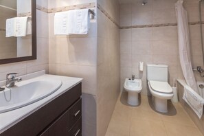 Een badkamer met een wastafel, bidet, toilet en douchegordijn.