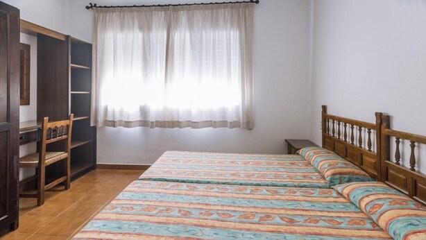 Une chambre à coucher avec un lit, une armoire, une chaise et une fenêtre avec des rideaux.