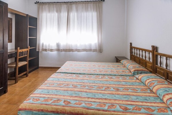 Ein Schlafzimmer mit Bett, Schrank, Stuhl und einem Fenster mit Vorhängen.