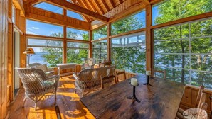 A wooden cabin with large windows, wicker furniture, and a view of the lake.