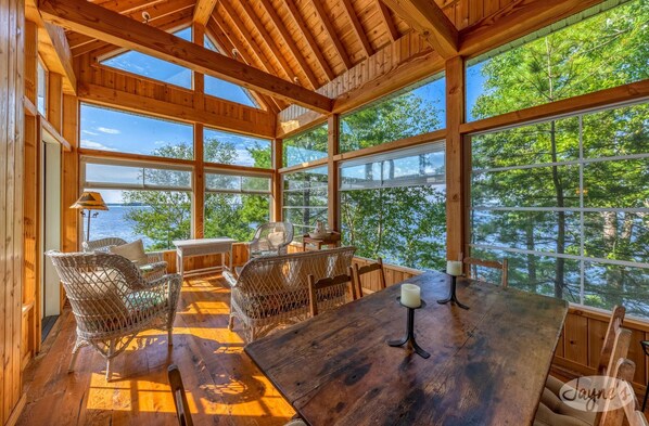 A wooden cabin with large windows, wicker furniture, and a view of the lake.