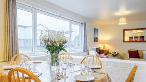 A dining area with a table set for six, a vase of flowers, and a view of the outside through large windows. - 3 bedroom accommodation in Brancaster Staithe, near Wells-next-the-Sea (Brancaster Staithe, near Wells-next-the-Sea)