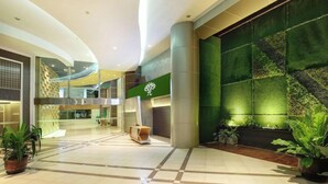 A modern lobby with a green wall, a reception desk, and potted plants. - Yuan Garden Pasar Baru (Jakarta)