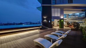 A modern outdoor lounge area with sun loungers, a pool, and a view of the city skyline at dusk. - Yuan Garden Pasar Baru (Jakarta)