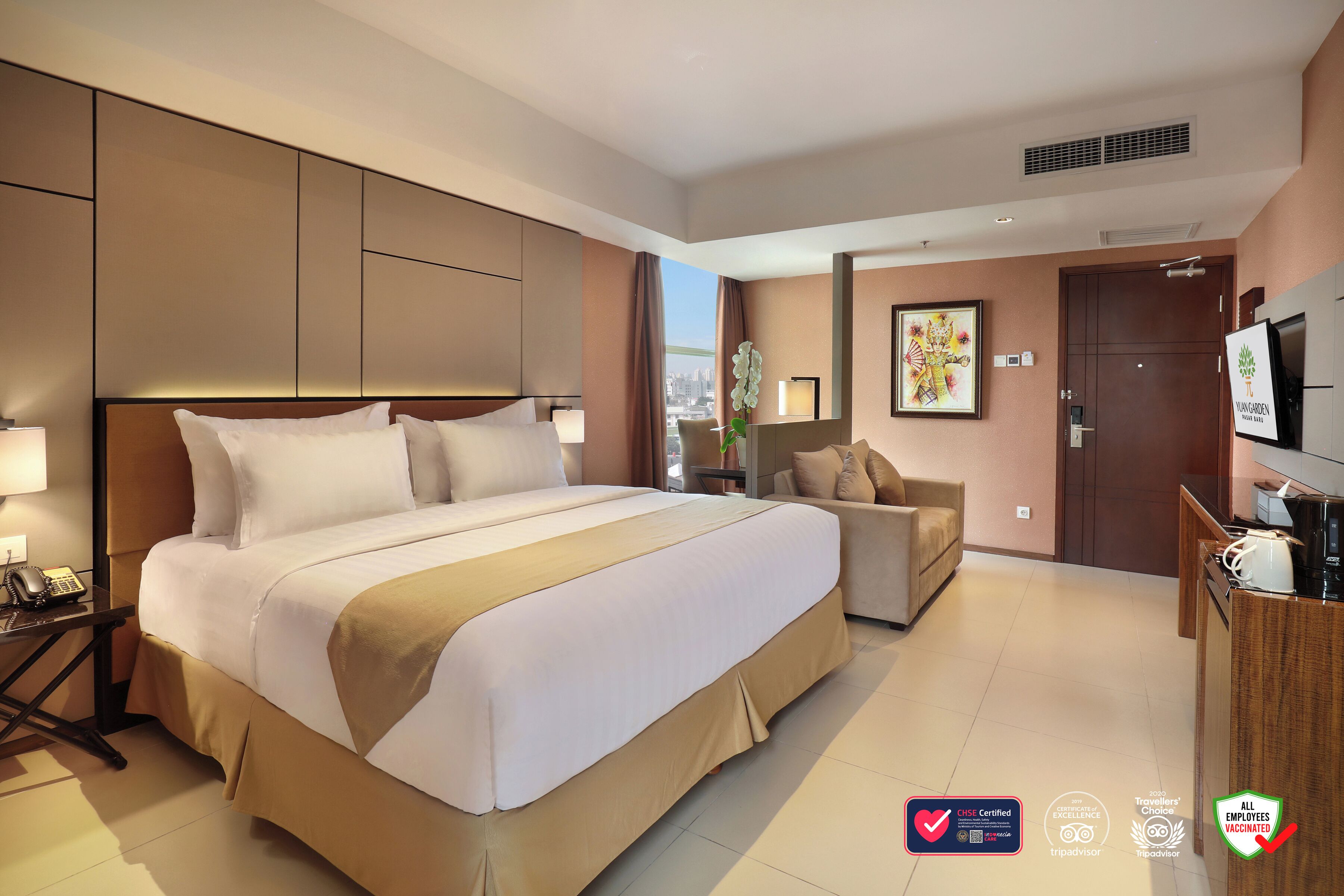 A hotel room with a large bed, a sofa, a TV, and a desk with a telephone.