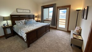 Un dormitorio con una cama grande, dos mesitas de noche, una mesita auxiliar, una ventana con cortinas y vistas al exterior.