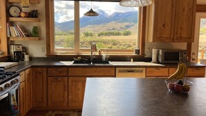 Una cocina con armarios de madera, un ventanal con vistas a la montaña, una lámpara colgante y un frutero sobre la encimera.