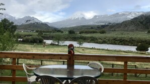 Una terraza de madera con una mesa y sillas, con vista a un río y montañas.