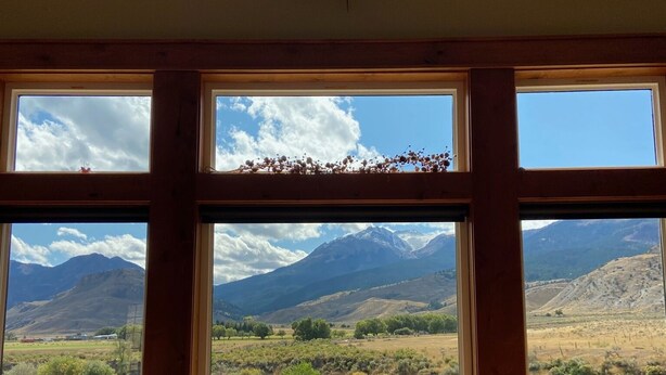 Habitación con amplios ventanales que ofrecen vistas a un río y montañas. Cuenta con un sofá de cuero y una mesa de madera.