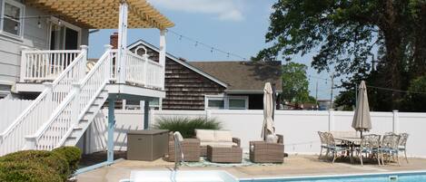 A residential pool area with a wooden deck, outdoor furniture, and a pergola.
