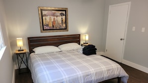 Cama bem arrumada com colcha xadrez, duas luminárias de cabeceira, um quadro emoldurado acima da cama e cabeceira de madeira.