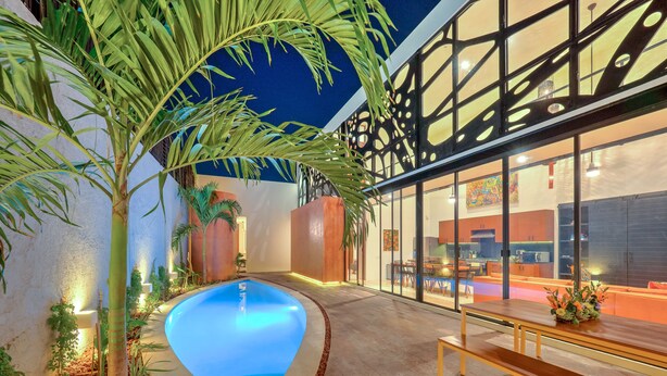 A modern building with a swimming pool, outdoor seating, and a well-lit interior.