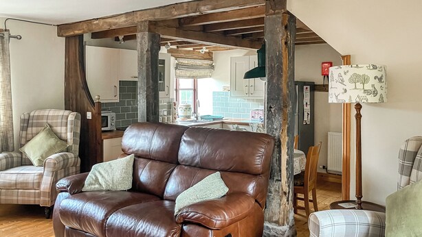 A living room with a brown leather sofa, plaid armchairs, and a wooden floor.