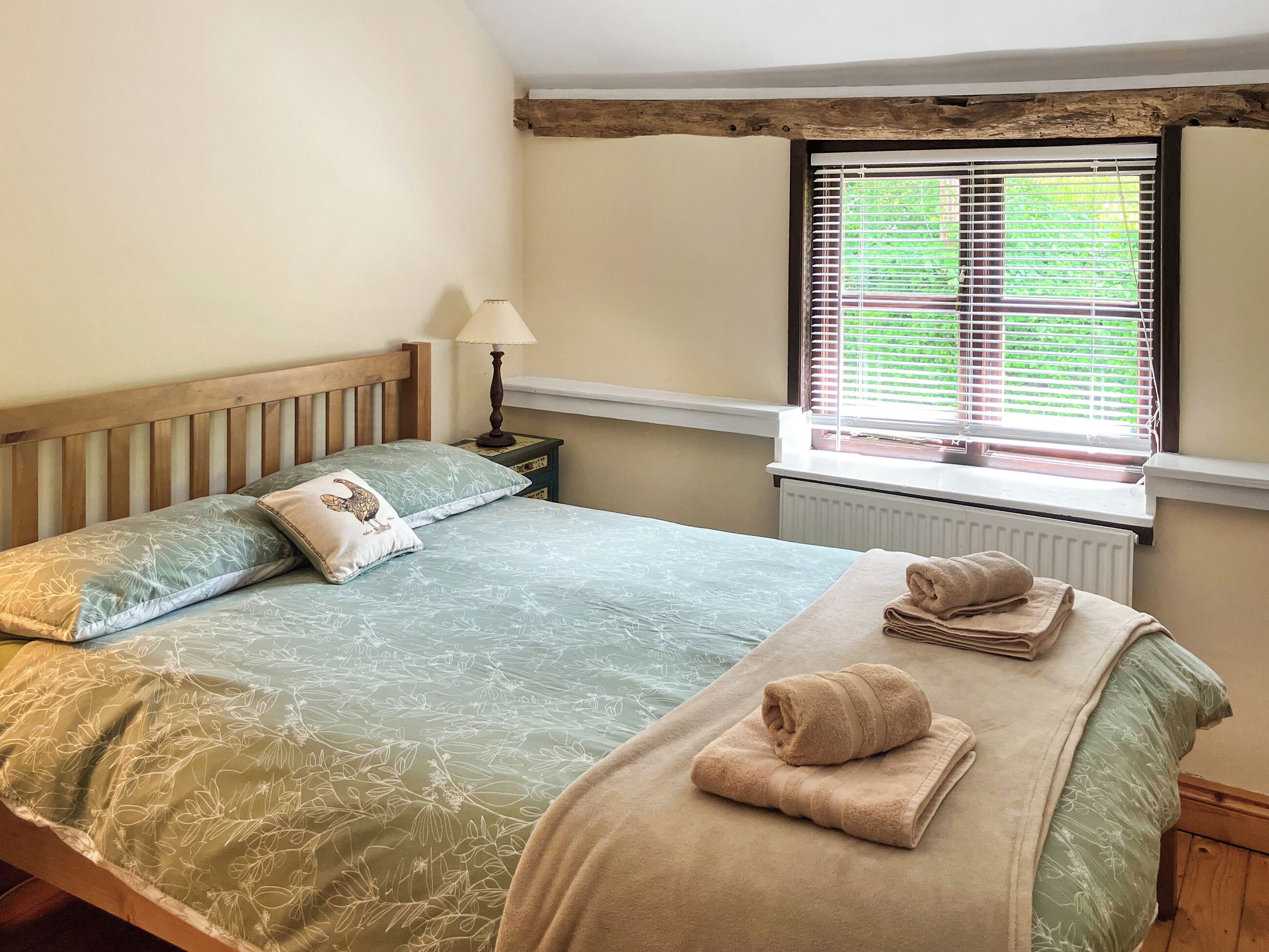 A bedroom with a bed, pillows, a lamp, a window with blinds, and a radiator.