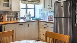 A kitchen with wooden beams, a stainless steel refrigerator, a window with a view, and a sink with a kettle.