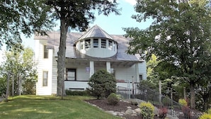 A two-story house with a gabled roof, a covered porch, and a well-maintained front yard with a lawn, shrubs, and a small tree.