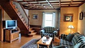 A living room with a wooden staircase, a television, a sofa, and a lamp.