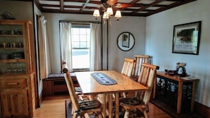 A dining area with a wooden table and chairs, a chandelier, and a view of the outdoors through a window.