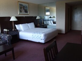 Habitación de hotel con una cama grande, lámparas de noche, teléfono, una silla, una mesa y un cuadro en la pared.