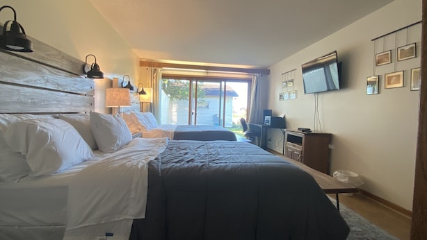 Quarto com cama grande, escrivaninha, televisão e porta de vidro deslizante para uma varanda.