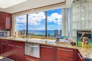 A kitchen with a large window overlooking a cityscape and the ocean.