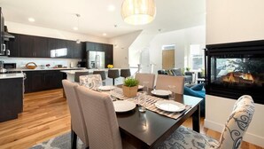 A modern kitchen with dark cabinetry, a central island, and a dining area with a table set for four. - Remarkable home near Old Town, Breweries, & River! (Fort Collins)