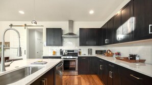 A modern kitchen with dark cabinets, stainless steel appliances, and a wooden floor. - Remarkable home near Old Town, Breweries, & River! (Fort Collins)