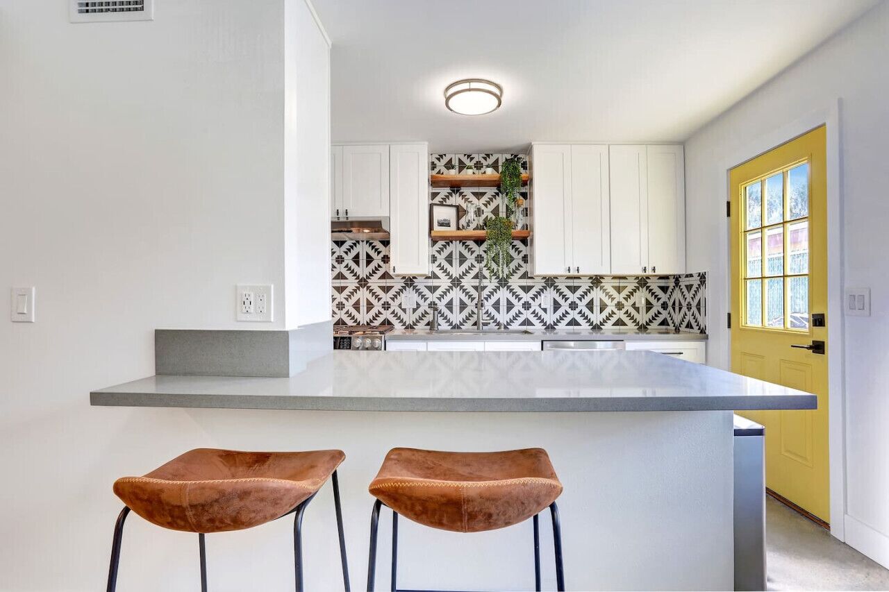 A modern kitchen with white cabinets, a patterned backsplash, and a large island with bar stools.