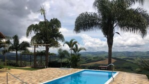 Ein rechteckiger Swimmingpool mit Fliesen und einer Sonnenterrasse, umgeben von Palmen und Blick auf sanfte Hügel.