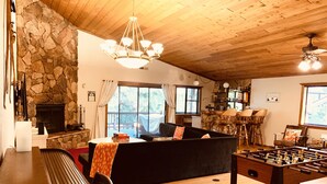 A cozy living room with a stone fireplace, a sofa, a foosball table, and a wooden ceiling. - The Bear Slumbers in Big Bear, spa, WiFi, foosball, pool/ping-pong (Big Bear)