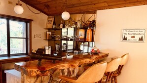 A rustic bar area with wooden chairs and a stone counter, a coffee machine, and shelves with bottles and glasses. - The Bear Slumbers in Big Bear, spa, WiFi, foosball, pool/ping-pong (Big Bear)