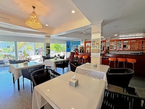A restaurant with tables and chairs, a bar area, and large windows with a view.