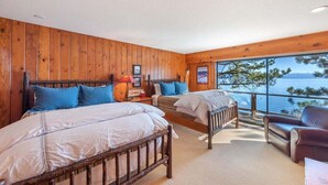 Un dormitorio tipo cabaña con dos camas de madera, cabeceros de madera y un ventanal con vistas a un lago.