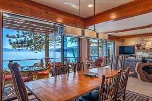 Enjoy meals in this dining area with a large table and comfortable seating, offering views of a serene body of water and distant mountains.
