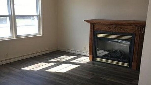 Ein Zimmer mit dunklem Holzboden, einem Kamin und einem großen Fenster, das natürliches Licht hereinlässt.