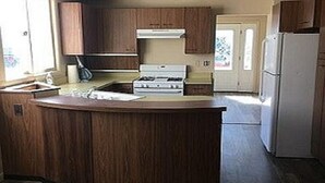 Eine kompakte Küche mit Holzausbau, einer zentralen Kochinsel, einem Herd und einem Kühlschrank.