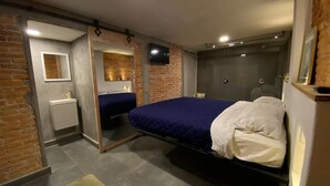 Une chambre à coucher comprenant un lit, une table de chevet, un miroir et un téléviseur fixé au mur.