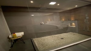 Une salle de bain moderne avec une douche à parois de verre, un banc en bois où sont posés les articles de toilette, et un grand miroir.