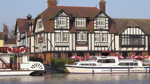 Edifici de planta tradicional en estil Tudor, amb un rètol que diu 'The Swan Inn' i una embarcació anomenada 'Delight' amarrada al davant.